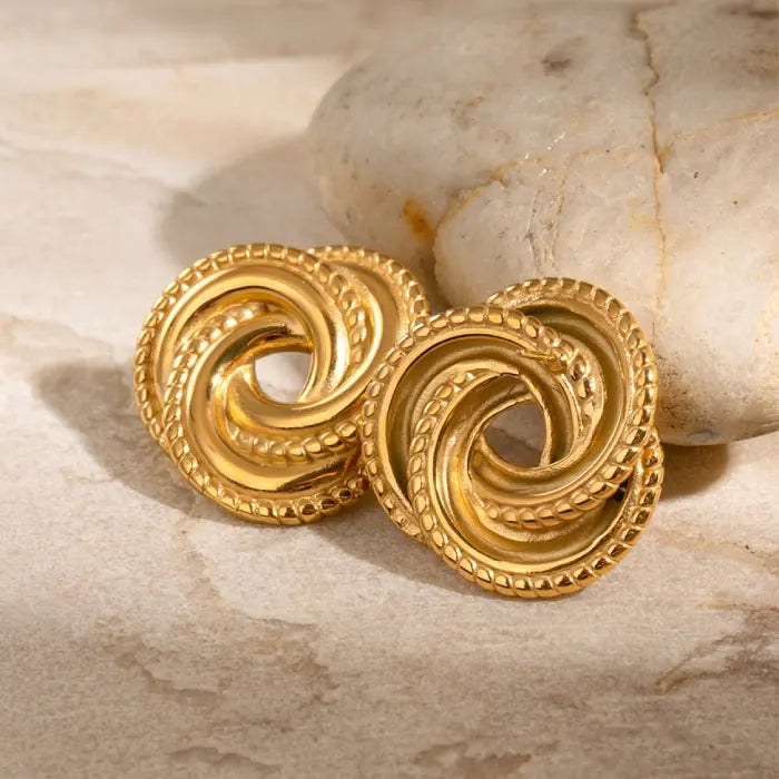 Gold statement knot earrings resting on marble stone, showcasing timeless and intricate jewelry design.