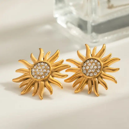 Gold sun-shaped stud earrings with crystal embellishments on a soft cream surface.