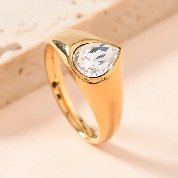 gold teardrop birthstone ring featuring a clear gemstone set in polished gold band, shown in bright close-up for detailed sparkle