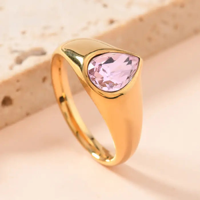 gold teardrop birthstone ring showcasing a bright red gemstone set in reflective gold, captured in a clean close-up for fine detail