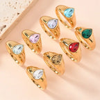 gold teardrop birthstone ring collection featuring multiple gemstone colors in polished gold settings arranged in a stylish display