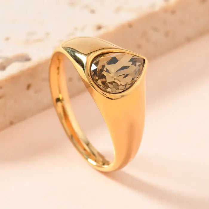 gold teardrop birthstone ring featuring a smoky quartz-style gem in a sleek gold band displayed in a warm, minimalist setting