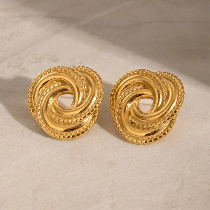 Elegant gold twisted knot earrings on a smooth beige surface, perfect for modern jewelry style lovers.