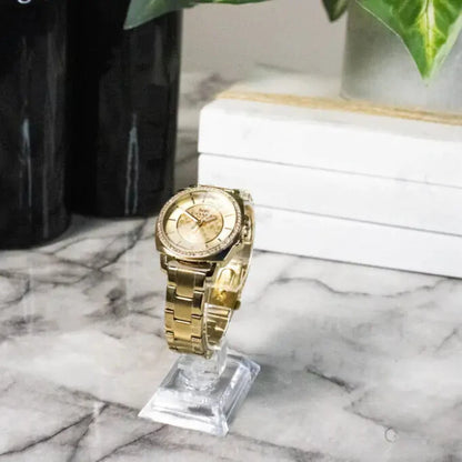 Gold-tone luxury watch on clear display stand against marble background