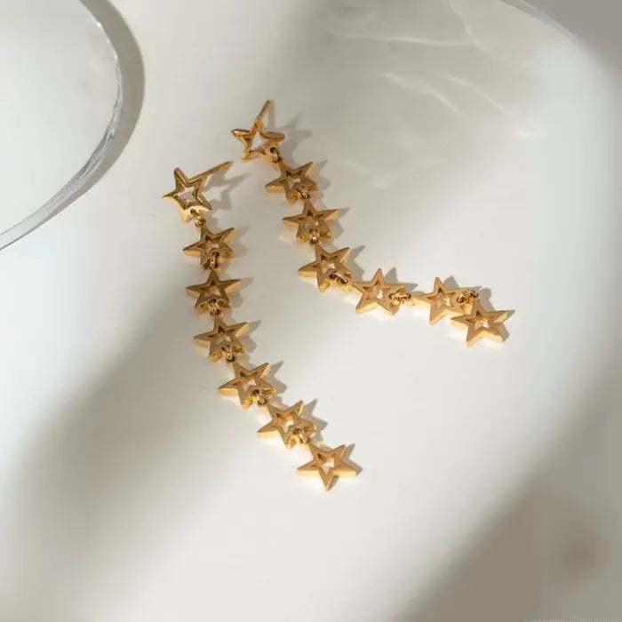 Elegant gold star chain earrings arranged on white surface with soft shadows