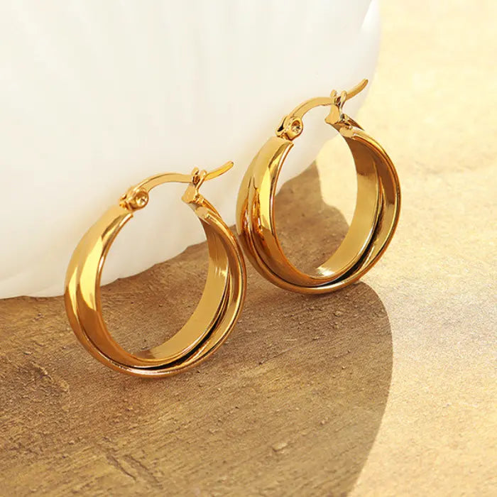 Classic golden hoop earrings on textured beige surface with dramatic shadows