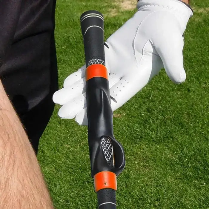 Golf training aid with black and orange grip held by gloved hand on grass