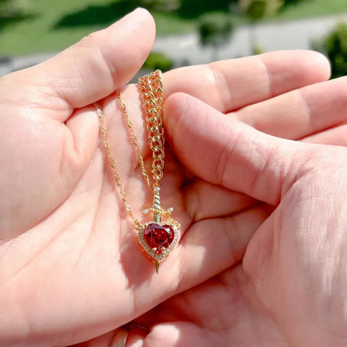 Gothic Heart Necklace held in hands with gold chain and deep red heart gemstone.