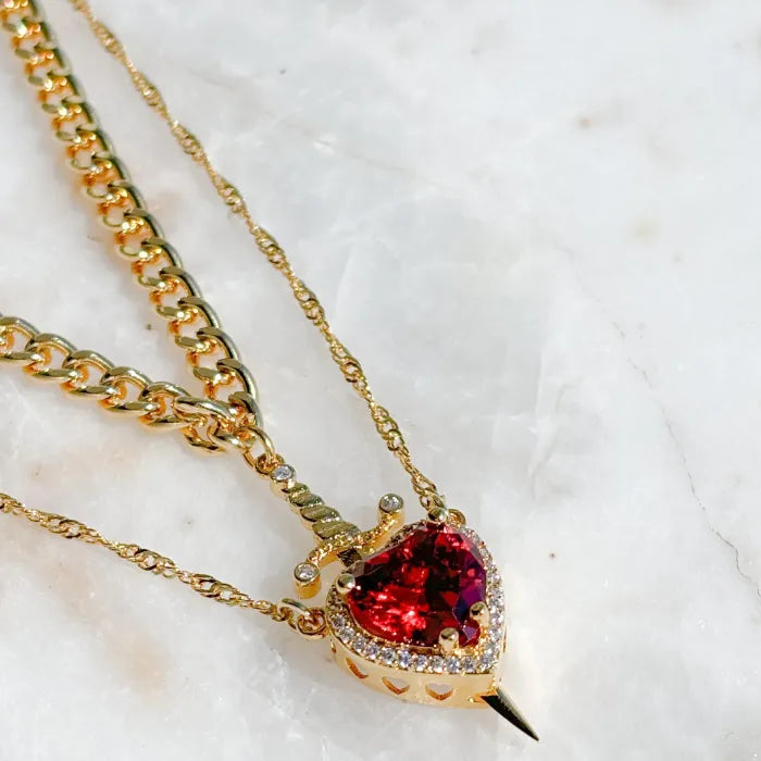 Gothic Heart Necklace on marble surface featuring gold chain and vivid red heart crystal.