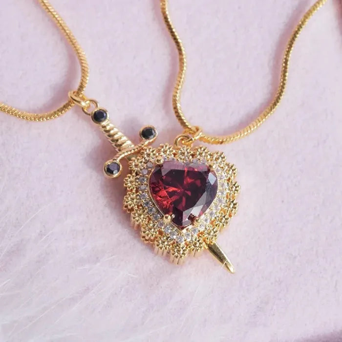 Gold necklace with a heart-shaped red gemstone pendant on a light pink background
