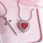 Gothic Heart Necklace with silver chain and red heart gemstone beside silver dagger pendant.