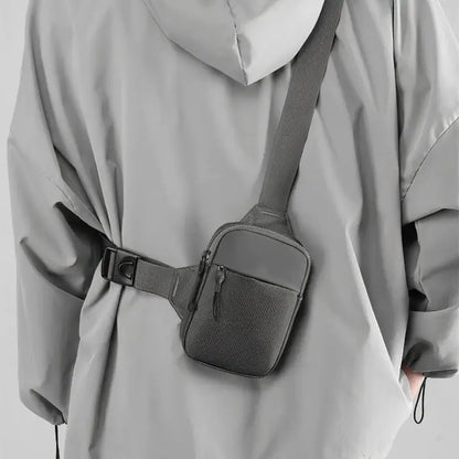 Person wearing gray chest bag with adjustable strap over light gray jacket, showcasing practical urban style