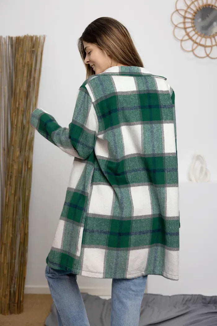 Back view of a woman wearing a green and white plaid wool coat paired with light blue jeans in an indoor setting.