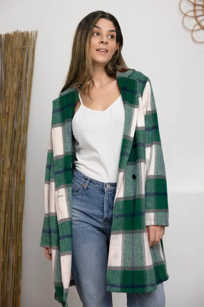 Woman in a green and white plaid wool coat styled with blue jeans and a white camisole in a minimal indoor setting.