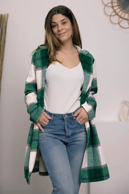 Woman wearing a green and white plaid wool coat styled with a white camisole and light blue jeans in an indoor setting.