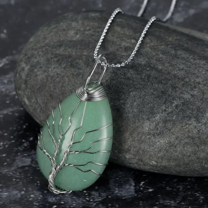 Green aventurine teardrop pendant with silver wire tree of life design on silver chain over dark stone.