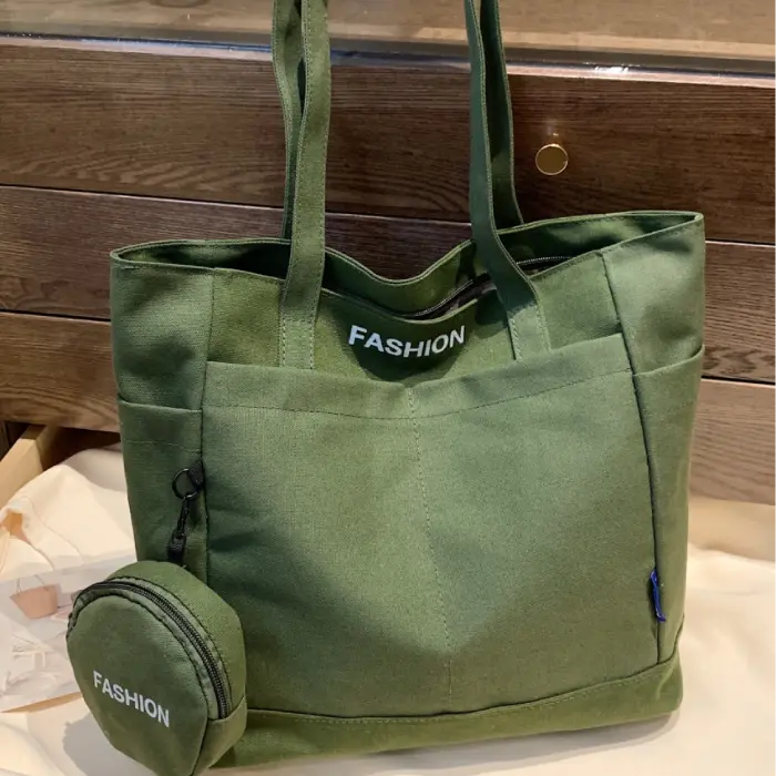 Olive green canvas tote bag with mini pouch labeled "FASHION," displayed on a wooden surface.