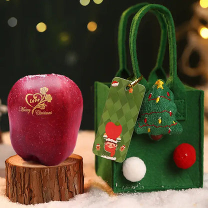 Green Christmas gift bag with a tree ornament, pom-poms, and a decorative apple nearby.