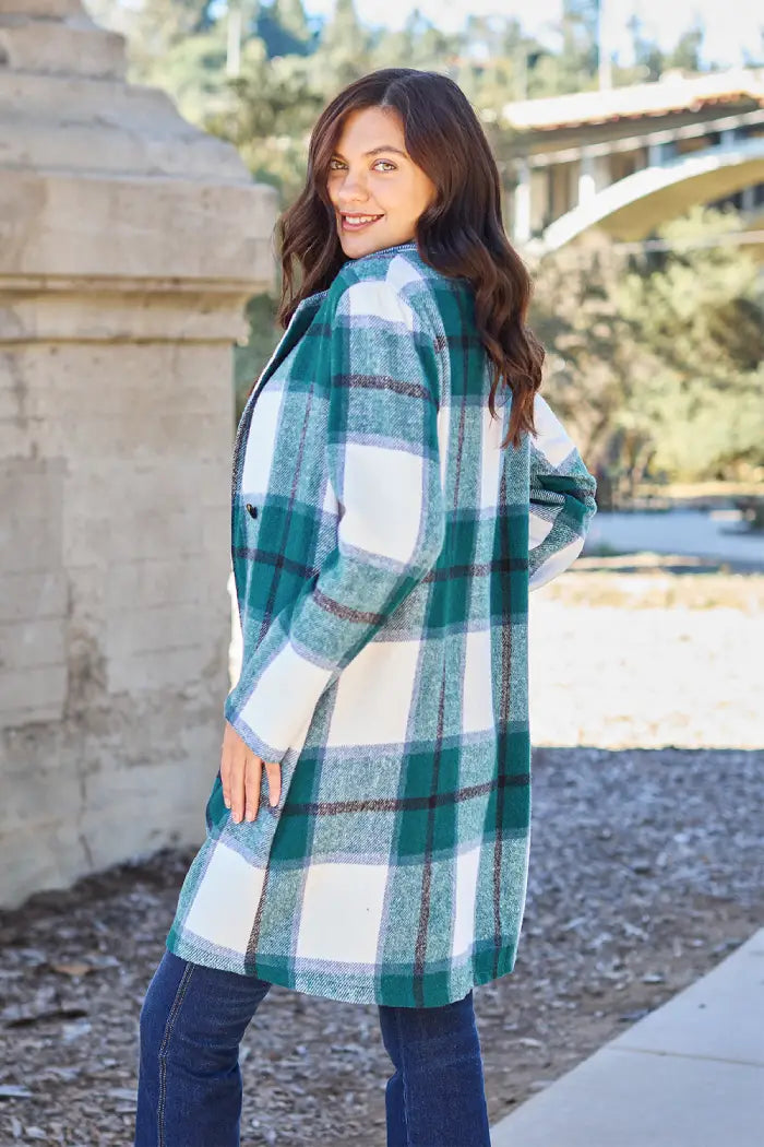 Woman showing the back view of a green plaid wool coat, styled casually with jeans in an outdoor park setting.