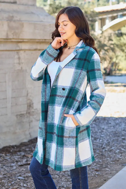 Woman in a green plaid wool coat with a single-button closure, styled with jeans and a white top in an outdoor setting.