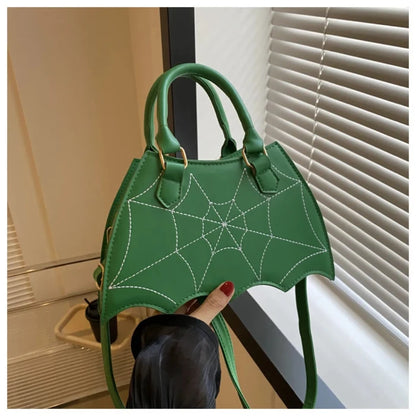 Green handbag with white spiderweb stitching, bat-wing shape, held by hand with red nails against white window blinds