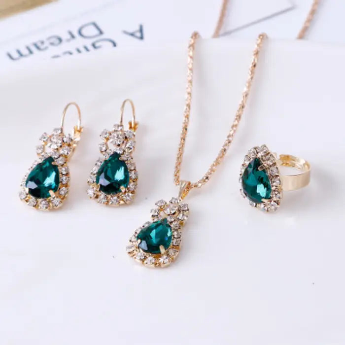 Teardrop-shaped green gemstone jewelry set featuring gold necklace, earrings, and ring with crystals.