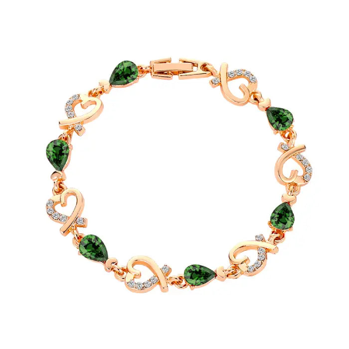 Gold plated bracelet with green teardrop gemstones and heart designs, sparkling with a luxurious aesthetic.