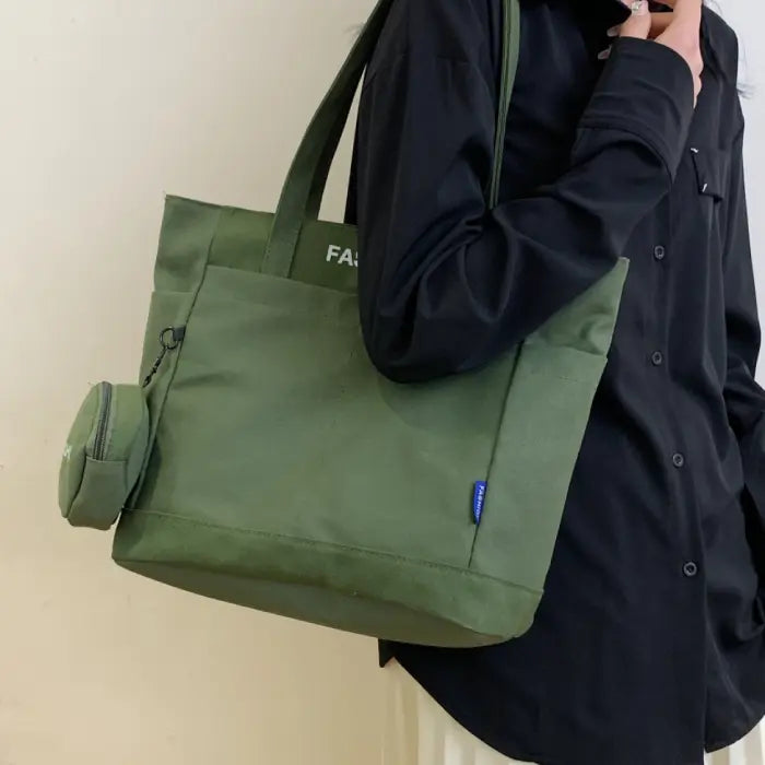 Stylish green tote bag with mini pouch, carried by a woman in a black shirt for a casual look.