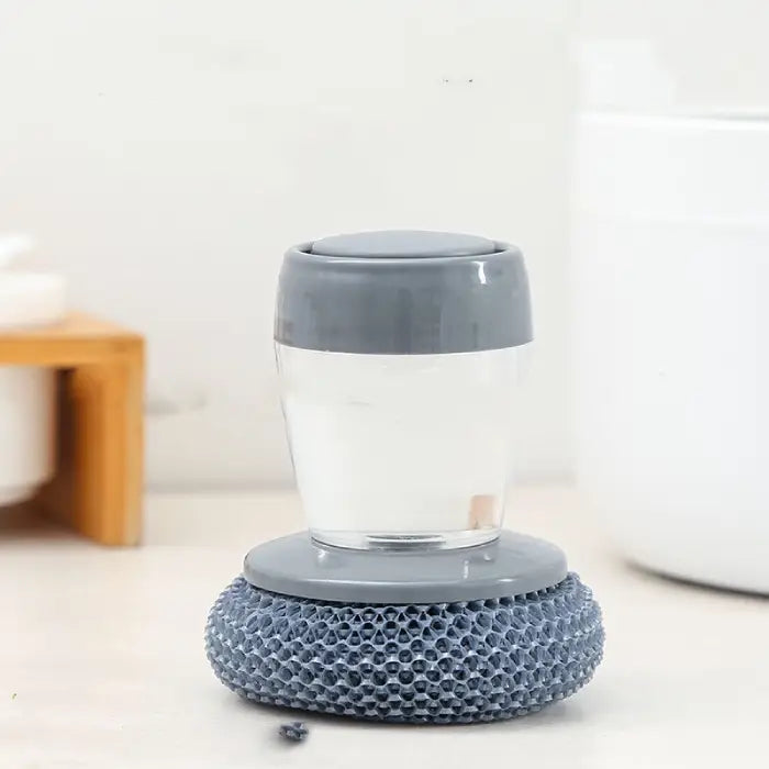 Grey soap-dispensing scrubber with a sponge base for efficient dishwashing and surface cleaning.