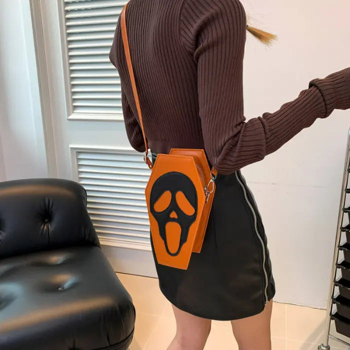 Halloween Coffin-shape Shoulder Bag in orange with black scream face worn with brown top and mini skirt