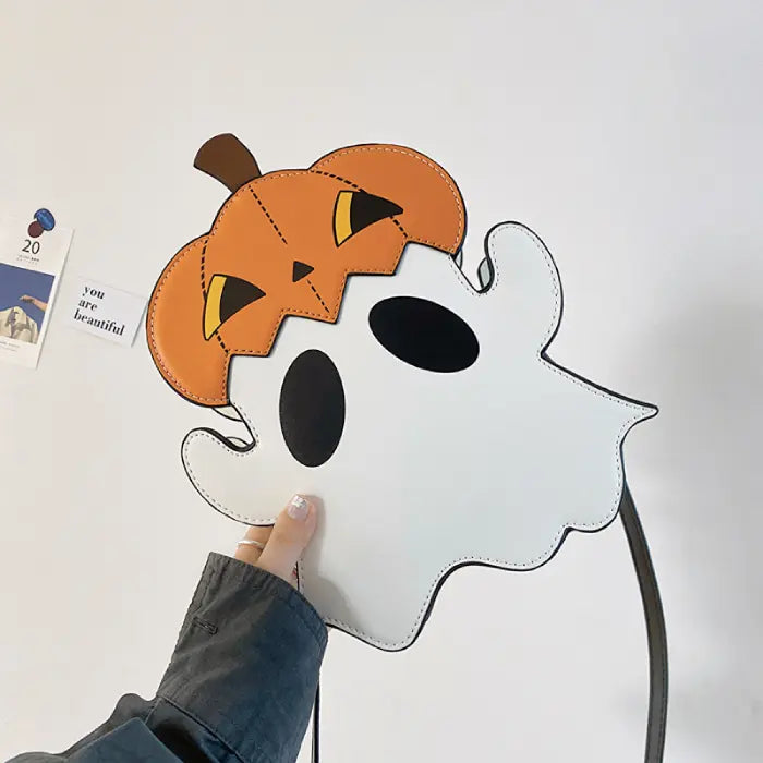Halloween crossbody ghost bag with pumpkin top held in hand against white background.