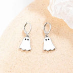 Silver hoop Halloween earrings with white ghost charms displayed on neutral textured surface.
