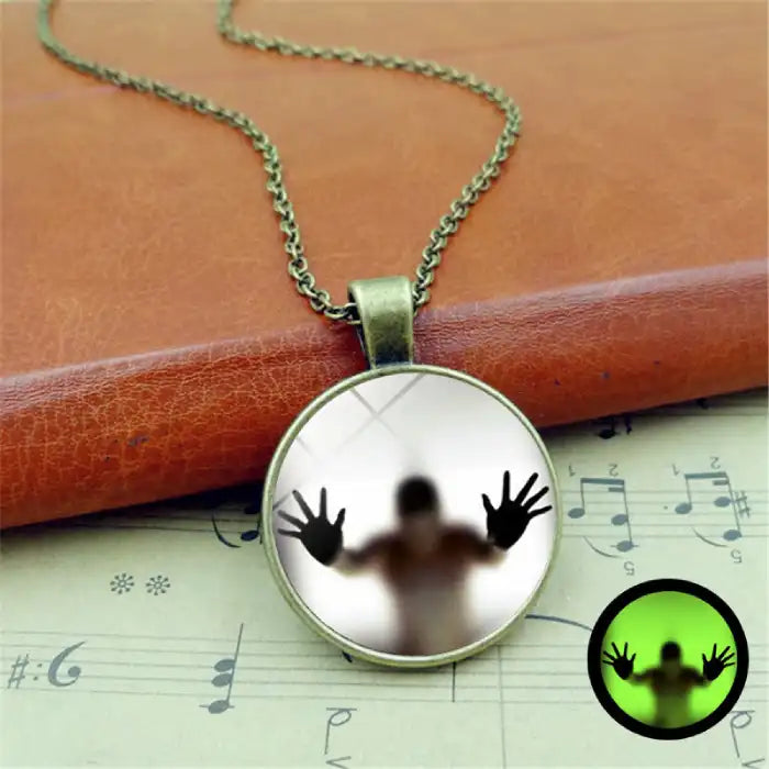 Halloween Glow necklace shown on vintage book with ghostly figure silhouette in round pendant.
