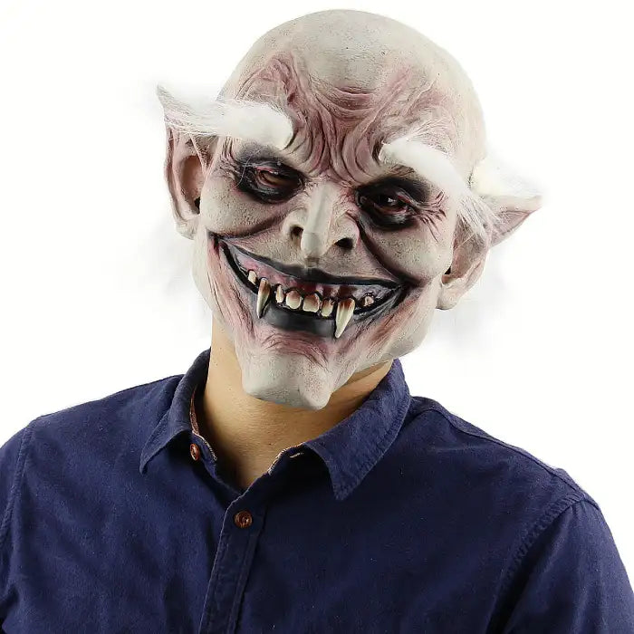 Halloween mask of grinning vampire goblin with fangs, white eyebrows, and wrinkled skin in close-up