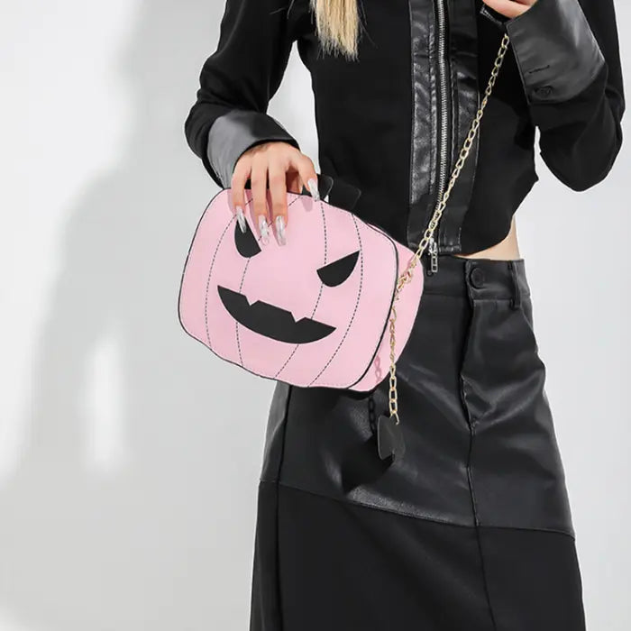 Pink Halloween Pumpkin Head bag with black face and gold chain held by woman in black outfit