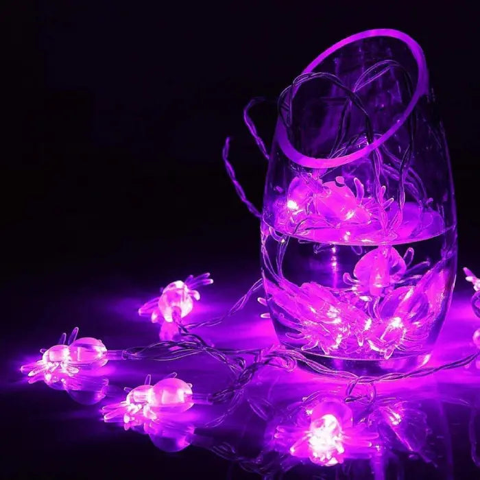 Halloween string lights with purple spider shapes coiled inside and around a glass vase
