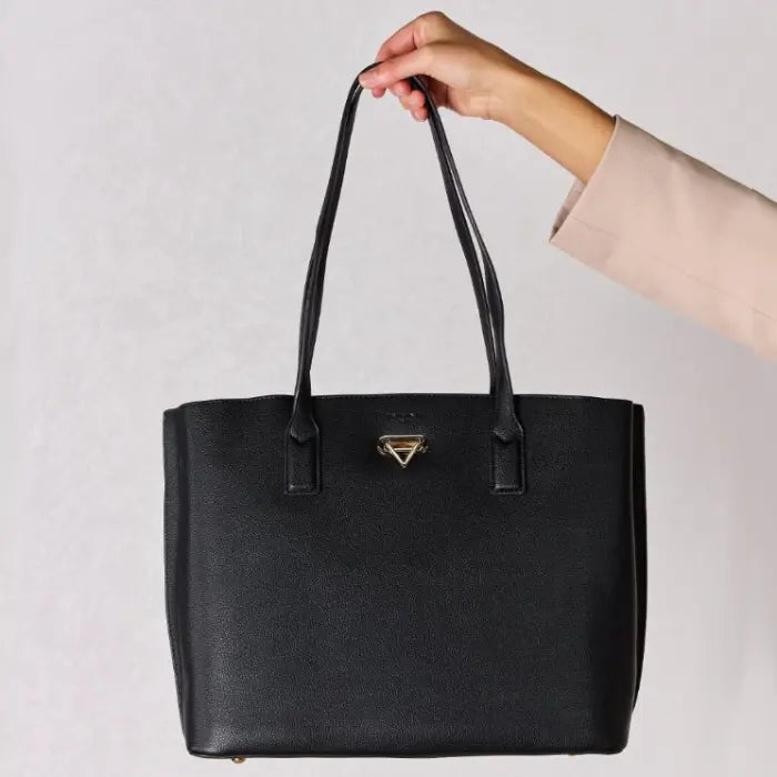 Hand holding a black leather tote bag by its straps, showcasing the bag's size and structure against a light background