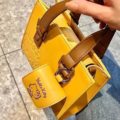 Close-up of hand holding yellow Hello Kitty handbag with brown straps and small front pouch for essentials.