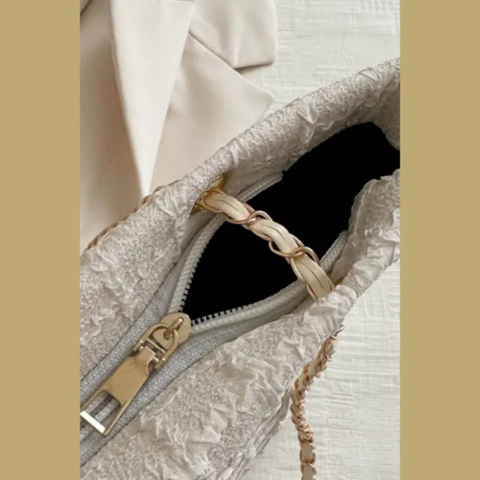 Close-up of cream textured handbag interior showing zipper and gold chain detail