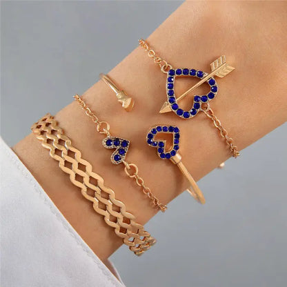 Gold bracelet set featuring heart designs, arrow motifs, and chain details with blue gemstone accents.