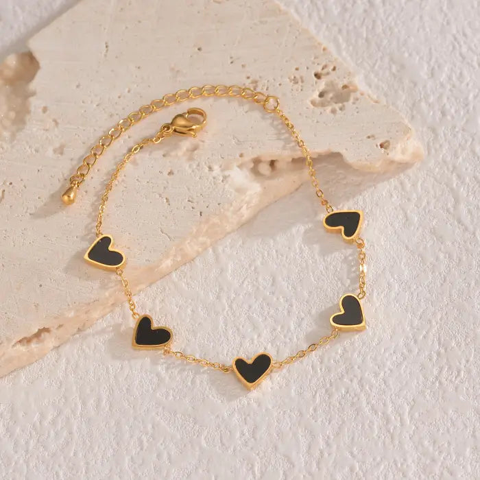 heart-charm-bracelet featuring black hearts on gold chain arranged on textured background, giving a bold classic style ideal for gifts
