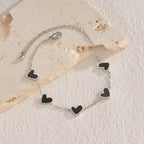 heart-charm-bracelet featuring black enamel hearts on silver chain laid on stone surface, giving a modern stylish look for gifting