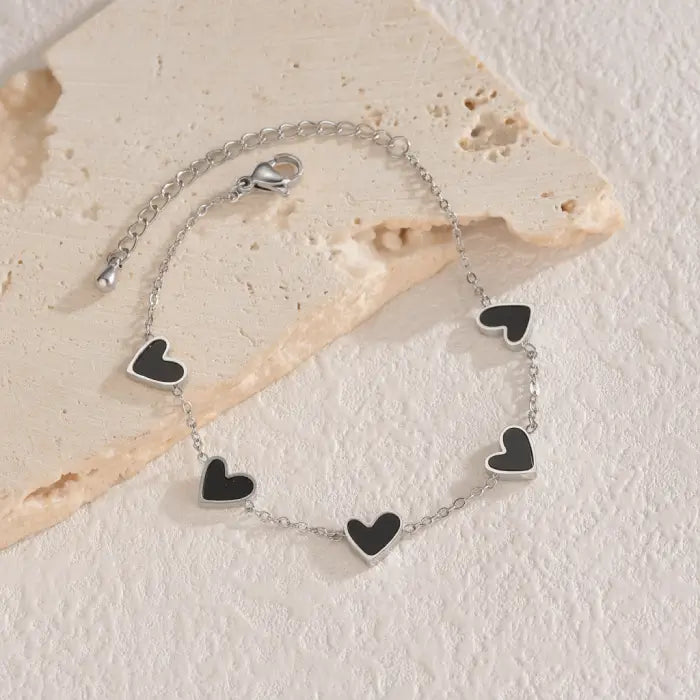 heart-charm-bracelet featuring black enamel hearts on silver chain laid on stone surface, giving a modern stylish look for gifting