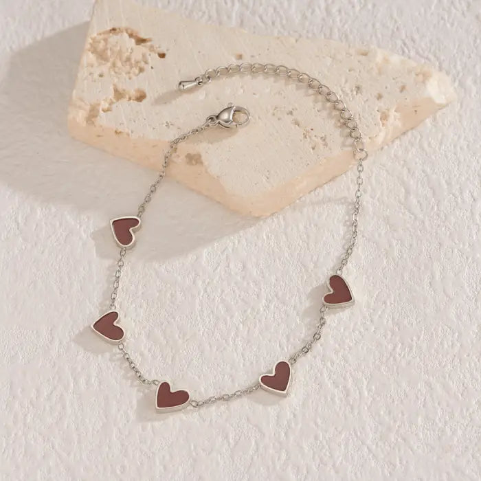 heart-charm-bracelet with brown enamel hearts on silver chain styled on textured surface, offering a warm trendy look for romantic gifts