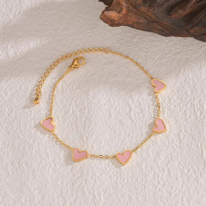 heart-charm-bracelet with pink hearts on gold chain displayed on textured surface, giving a soft romantic style ideal for 2025 gifting