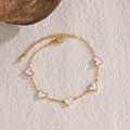 heart-charm-bracelet with white enamel hearts on gold chain displayed on textured surface, offering a premium minimalist jewelry look
