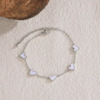 heart-charm-bracelet with white enamel hearts on silver chain displayed on textured surface, offering a clean minimalist jewelry style