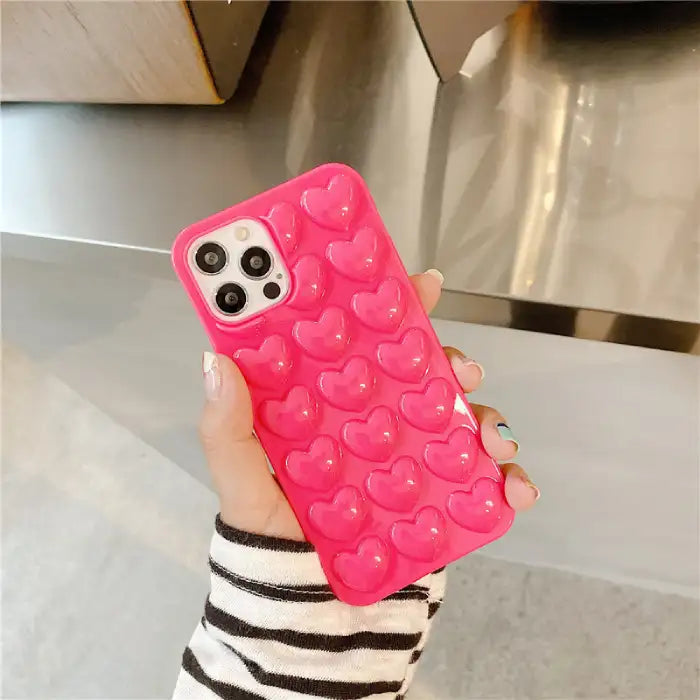 Heart iPhone case in vibrant hot pink featuring 3D raised heart pattern for enhanced grip and stylish protection