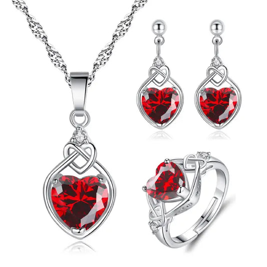 Elegant silver jewelry set with heart-shaped red gemstones featuring necklace, earrings, and ring.