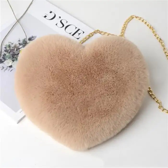 Beige heart shoulder bag in soft plush material with gold chain strap on white surface.